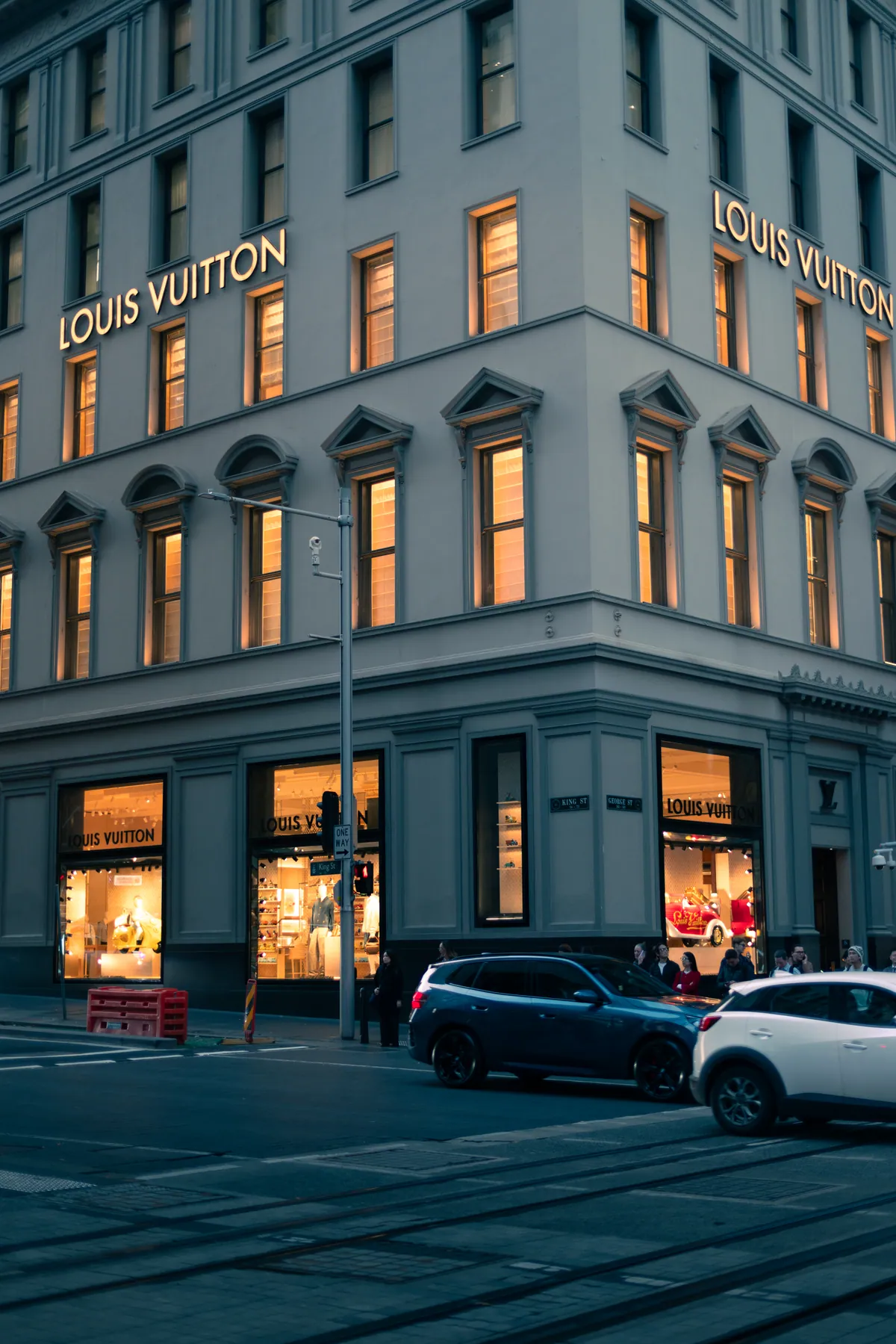 A heritage sandstone building with lit luxury shopfront windows on a city corner
