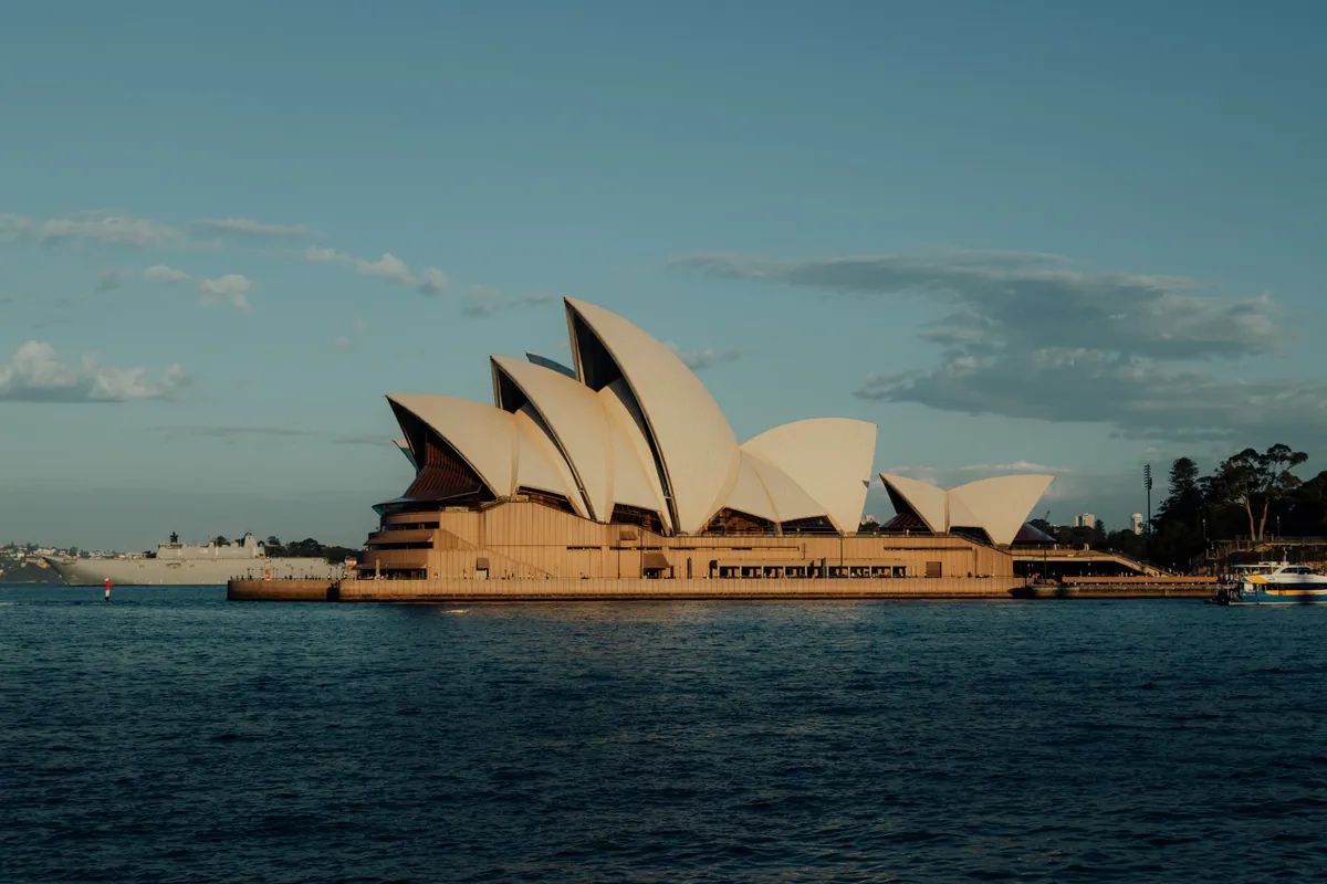The Opera House on Bennelong Point, sails lit warm against a blue sky