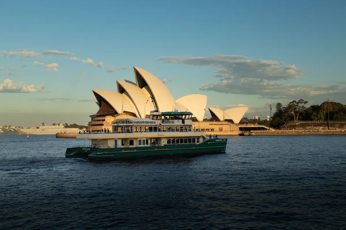 A green-and-cream harbour ferry crossing the harbour in front of the Sydney Opera House in late sun